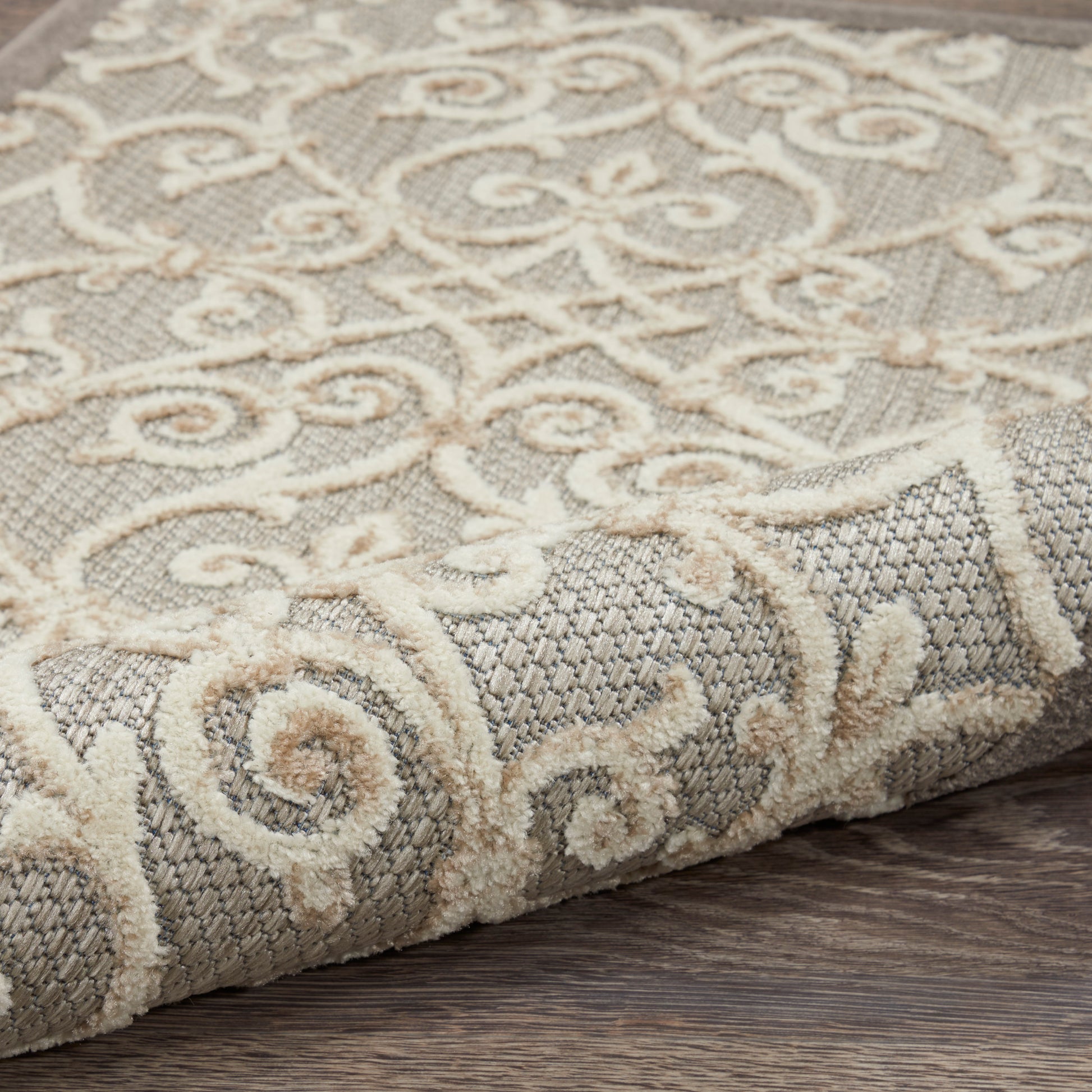 Gray & cream ornate scroll-pattern area rug, woven texture with cream motif, folded corner on wooden floor.