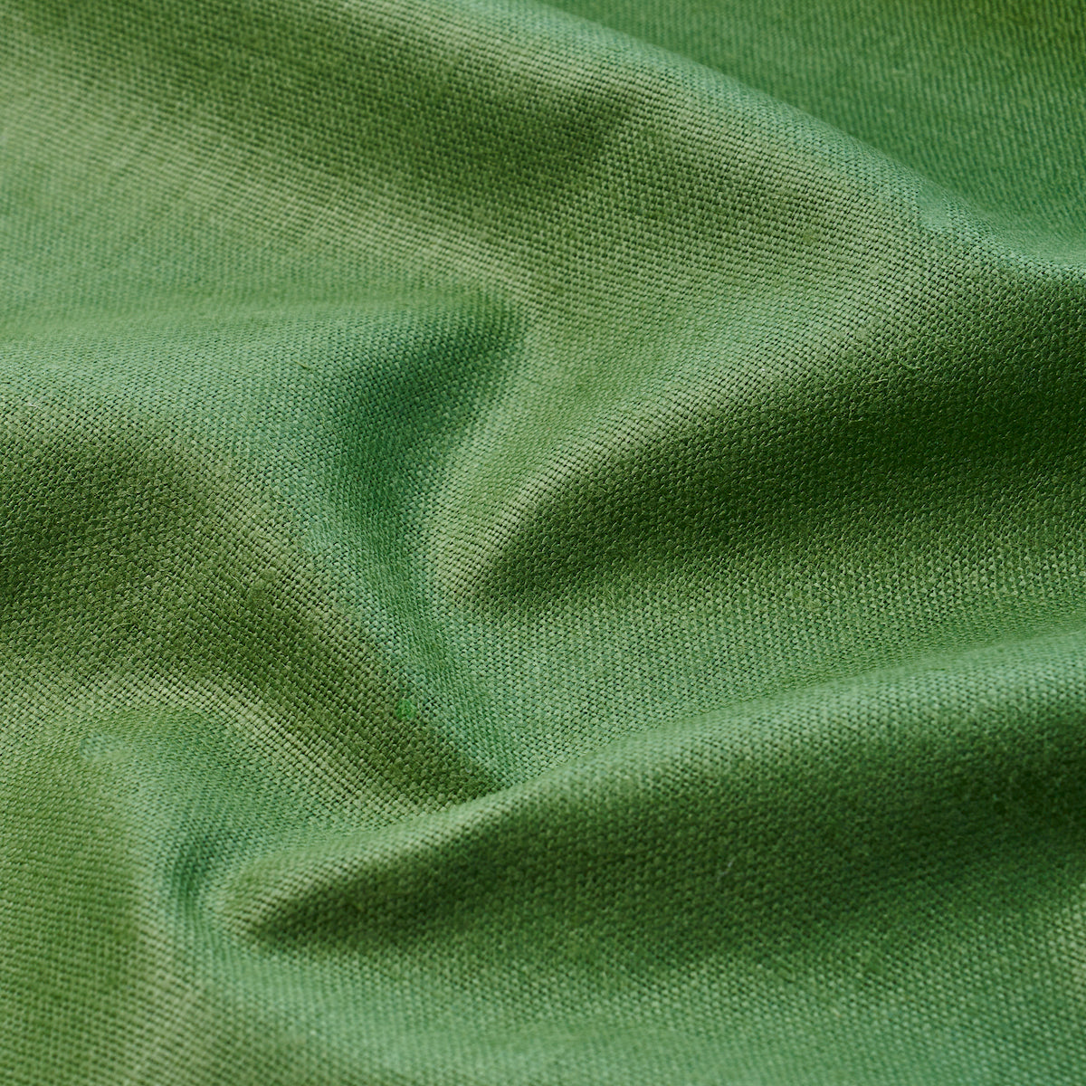Green linen fabric close-up with soft folds and fine weave, smooth drape.