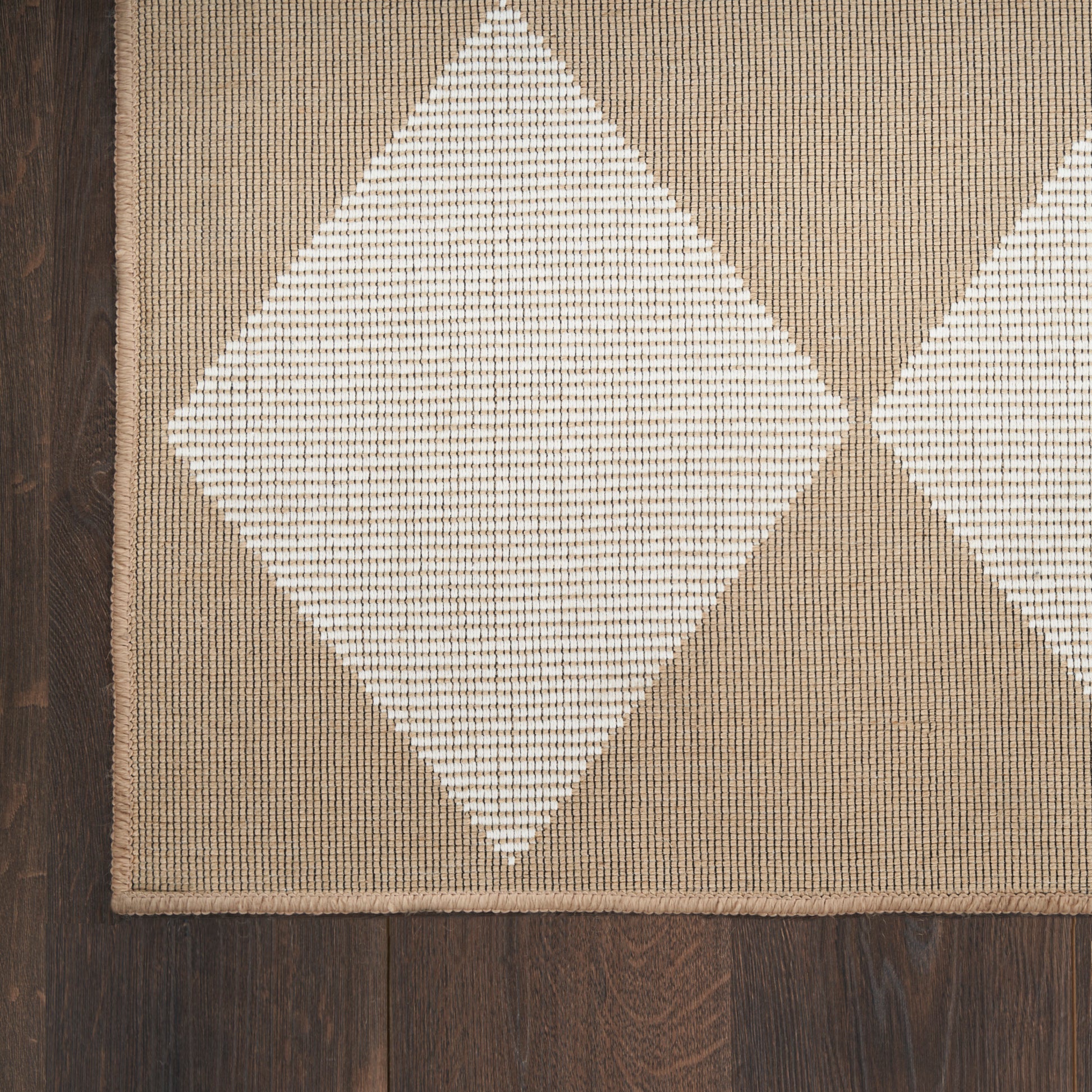 Beige-brown diamond-pattern rug with white diamonds, woven texture, bordered edge on dark wood floor.