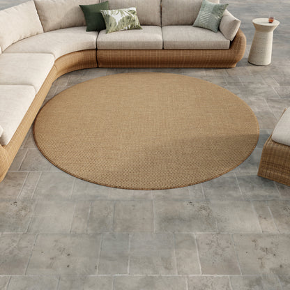 Round tan woven rug on gray tile, paired with beige modular wicker sofa and green cushions in a sunlit outdoor living area.