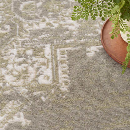 Beige-gray rug with white geometric pattern; green fern on round wooden tray in corner.