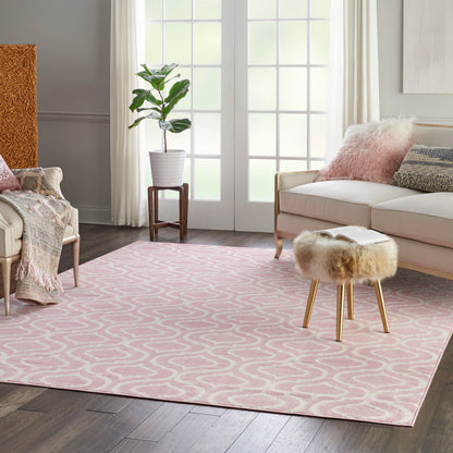 Pastel pink area rug with white geometric loops in a cozy living room; fur-stool, beige sofa, plant, & throw blankets.