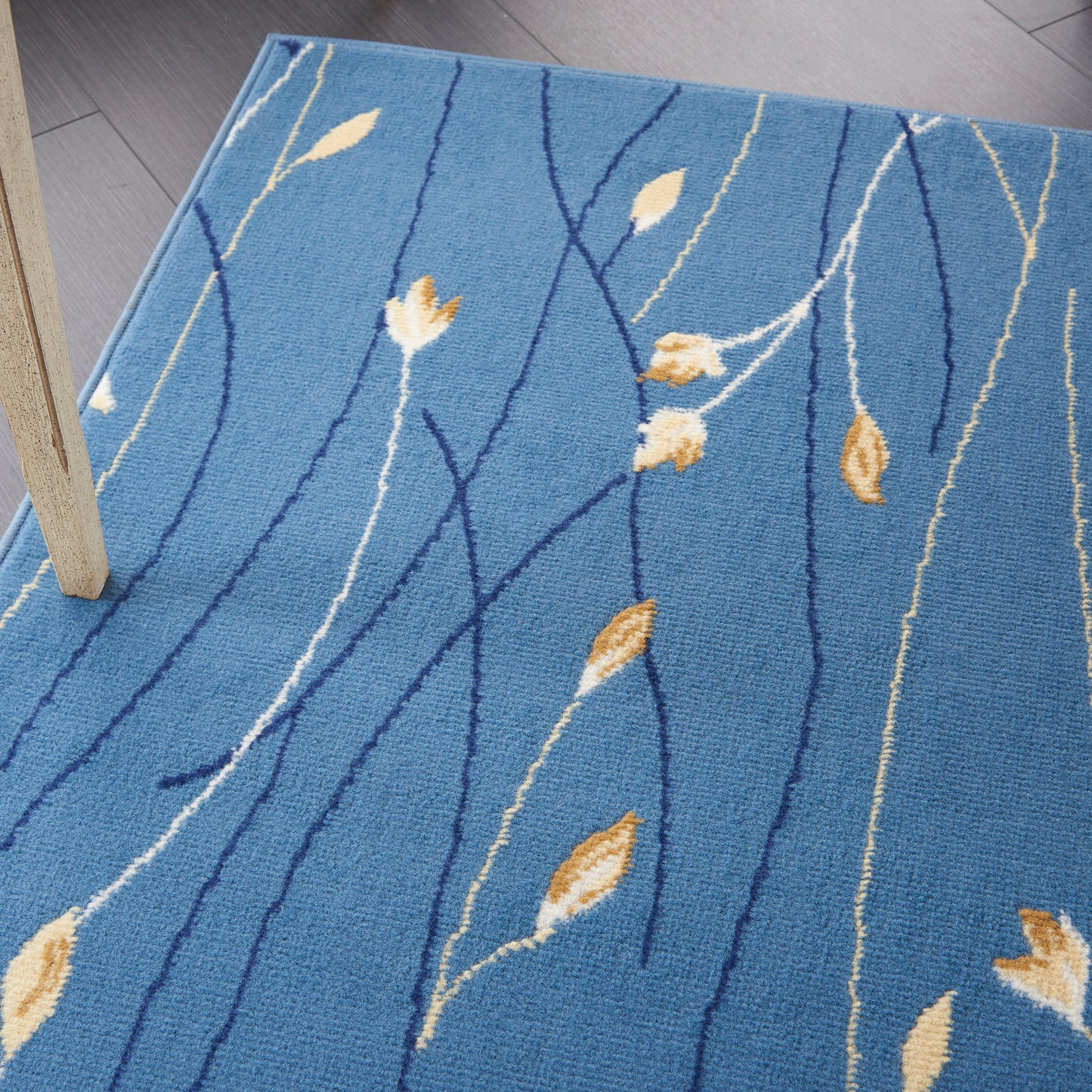 Blue rug with abstract dark blue curved lines and beige leaf motifs; partial wood furniture leg visible.