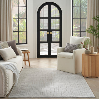 Light grey flatwoven area rug in a bright living room with cream sofa, neutral pillows, and an arched black door.