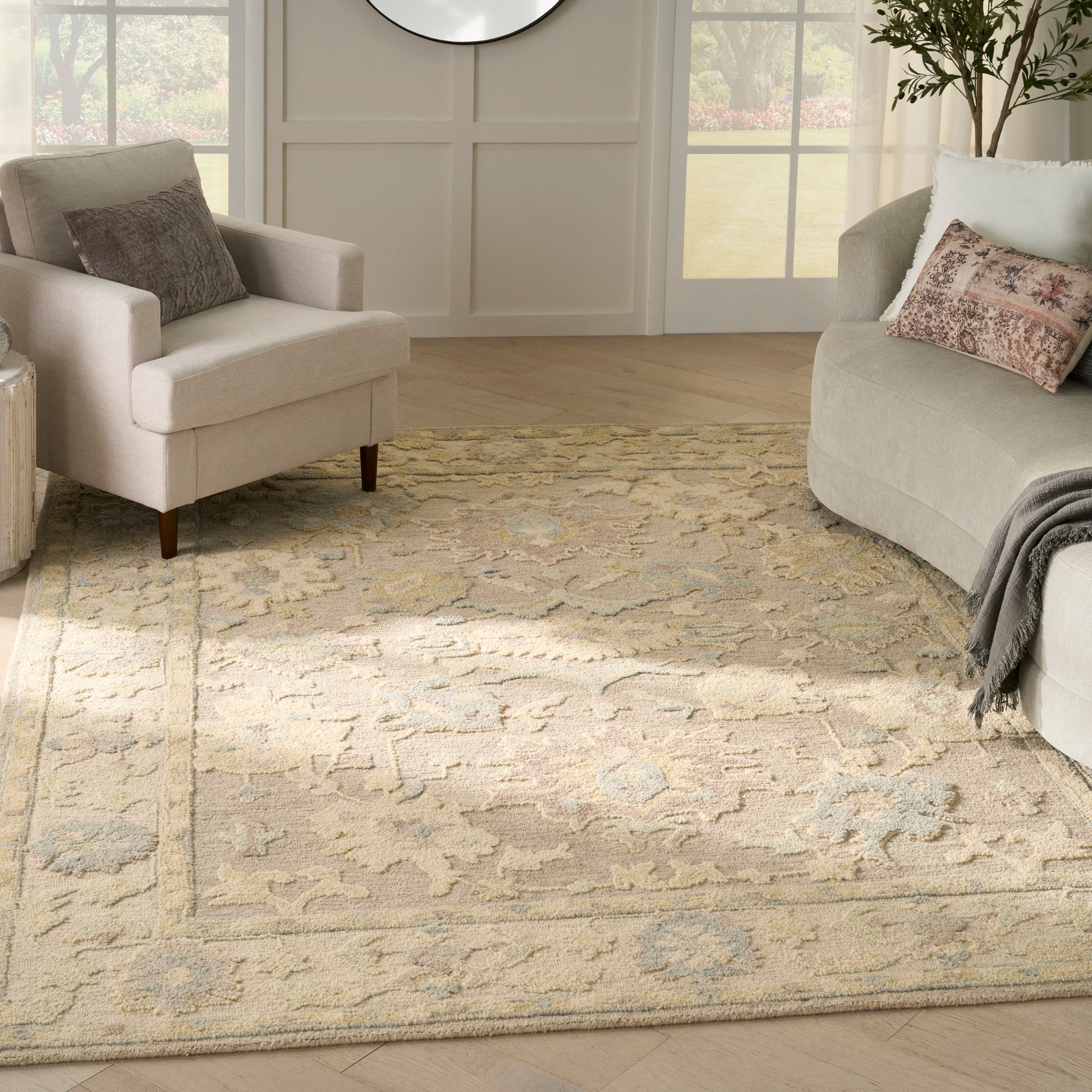 Cream sofa and chairs on a beige patterned area rug with pale blue accents in a bright paneled living room.