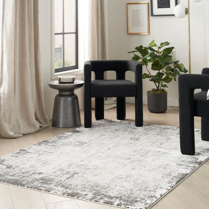 Modern living room with black boucle chairs, round metal side table, grey distressed rug, potted plant, & brass floor lamp.