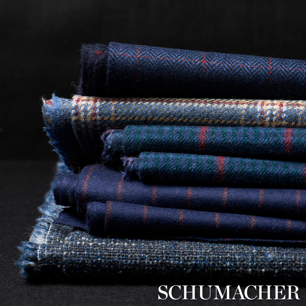 Stack of navy wool fabrics with plaid and tweed patterns, folded with fringe edges; Schumacher.