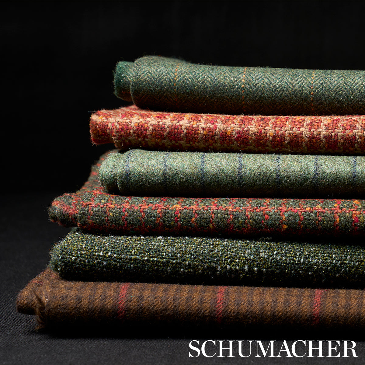 Stack of folded wool tweed fabrics in green, red & brown tones with plaid and striped patterns.
