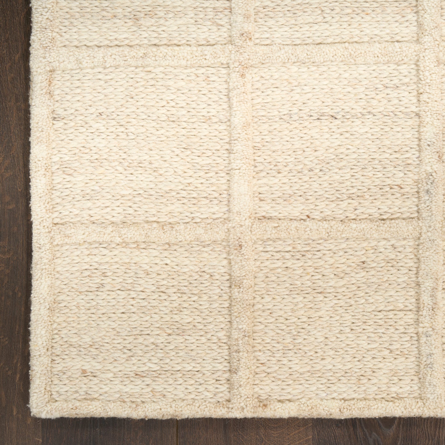 Beige woven rug with square block pattern and thick loop texture on dark wood floor.