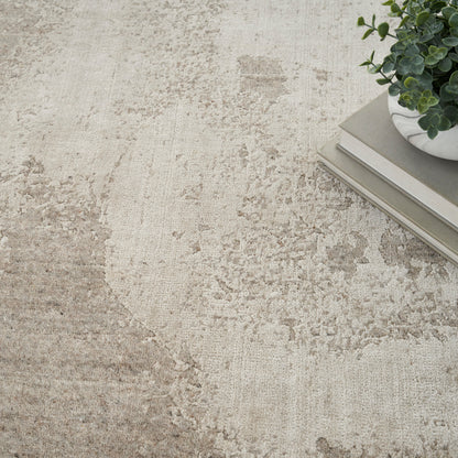 Beige textured rug with a white ceramic pot of eucalyptus and stacked neutral books in the top-right corner.