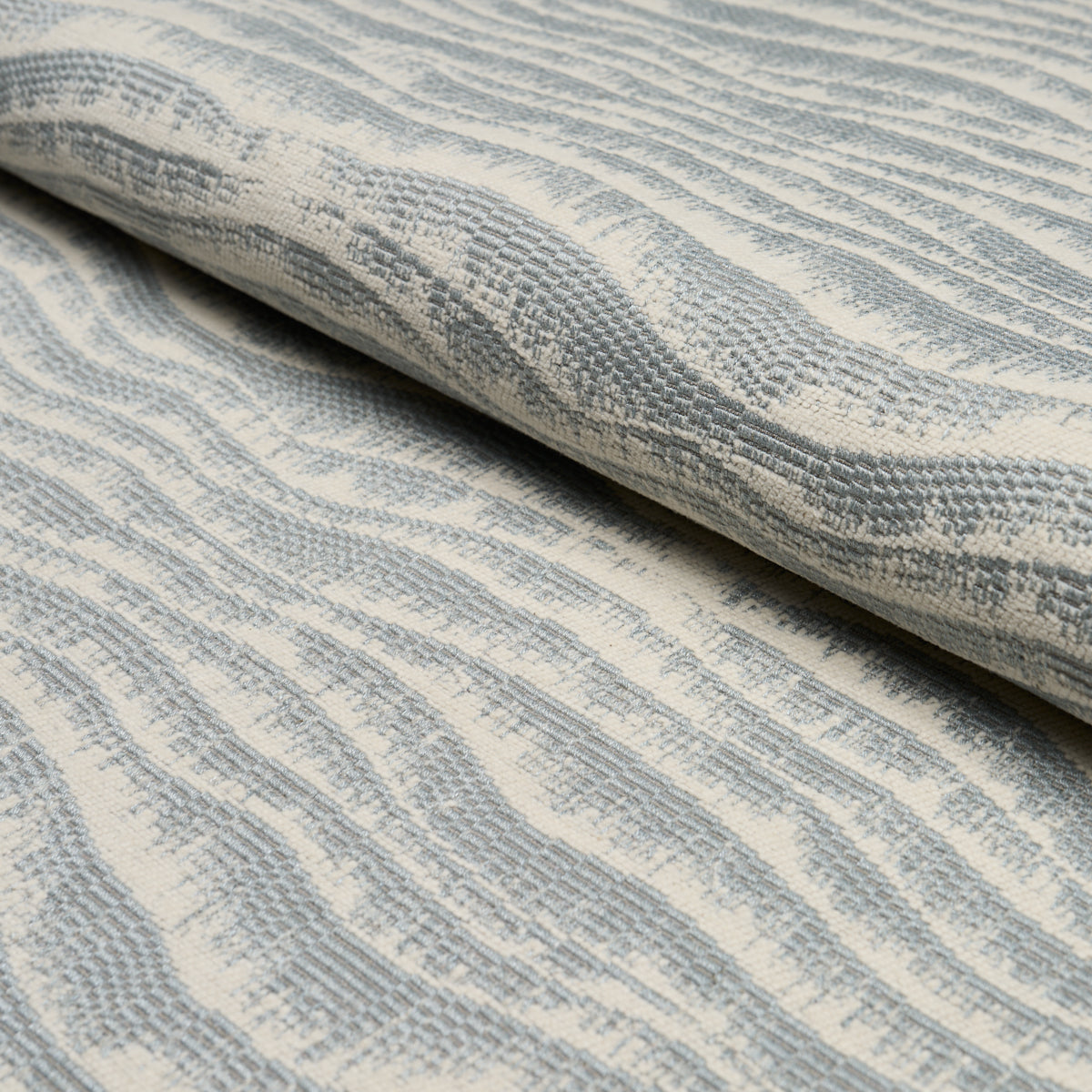 Rolled light blue and ivory woven fabric with soft, wavy stripe texture, ideal for upholstery or drapery.