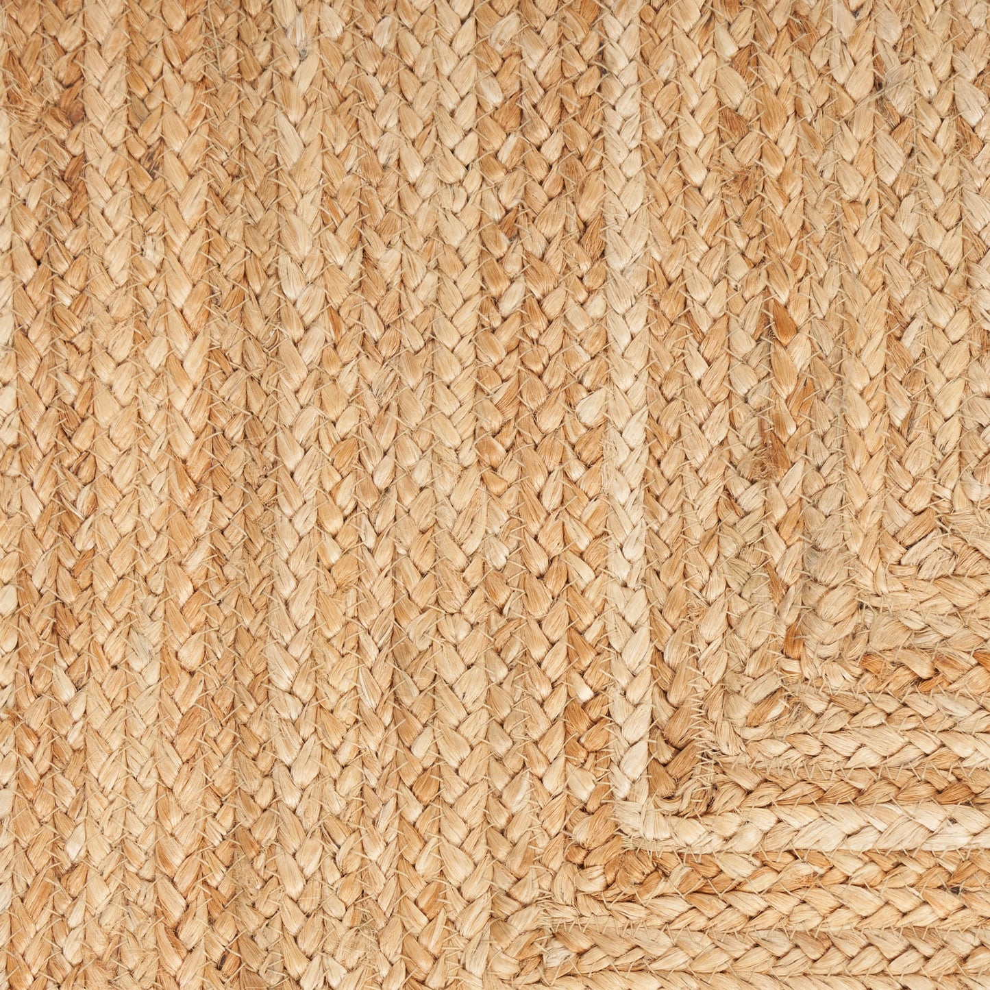 Close-up of natural jute rug with braided border, warm beige-brown woven fibers.