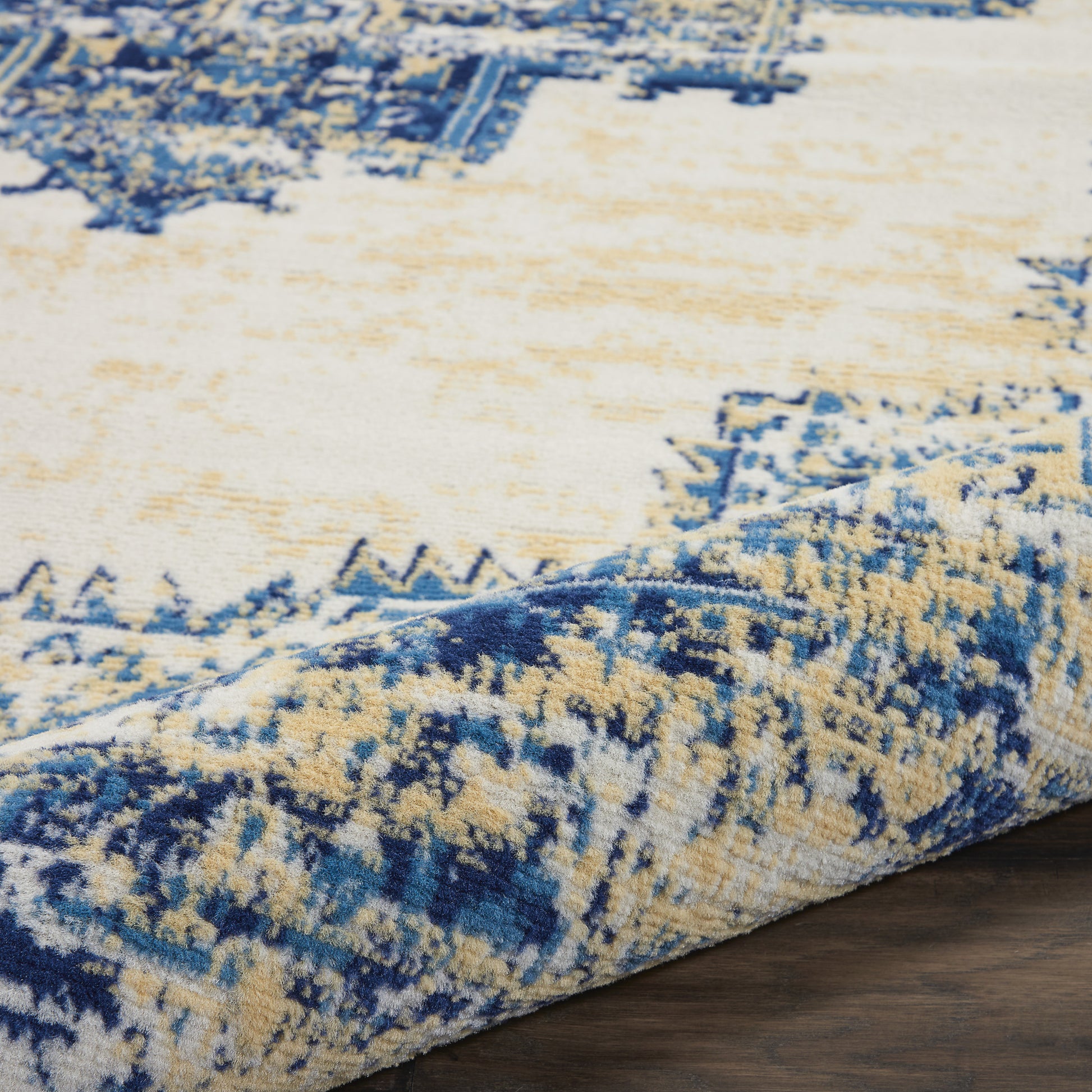 Blue and cream abstract patterned rug with plush pile and rolled edge on dark wood floor.