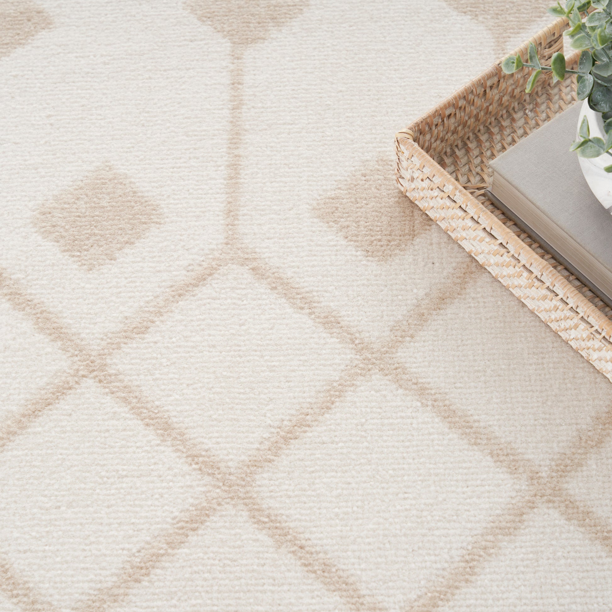 Beige textured rug with pale diamond lattice pattern; woven wicker tray in top-right holds books and a small plant.