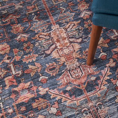 Blue oriental woven rug with pink, ivory & brown floral motifs; wooden chair leg resting on it.