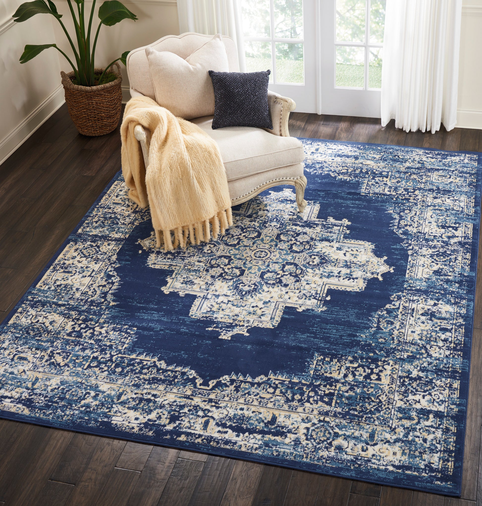 Navy and cream distressed oriental rug, 8' x 10', in a sunlit living room, with a cream tufted armchair, beige knit throw, and navy pillow nearby.