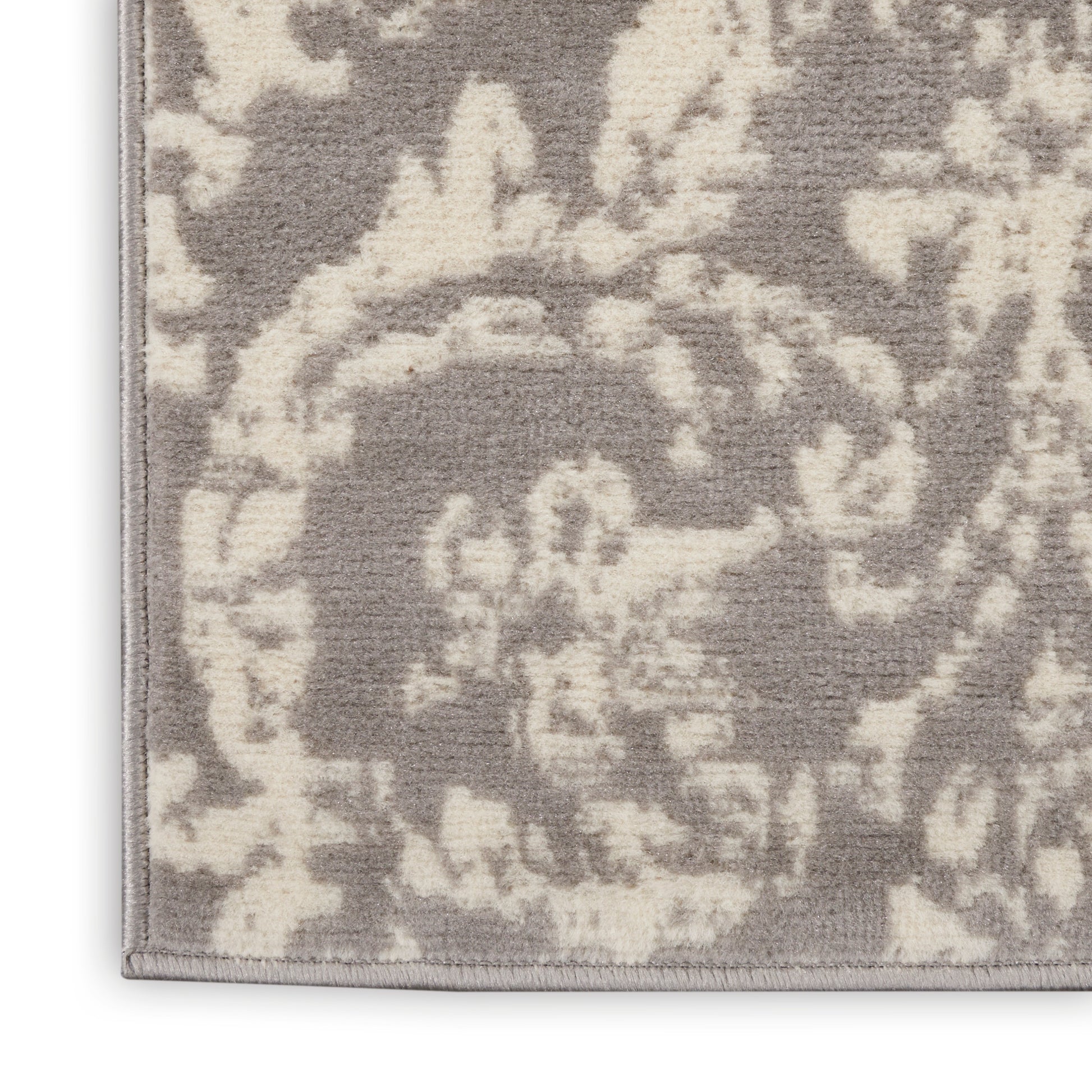 Corner of soft taupe and ivory damask rug with ornate floral pattern and bound trim.