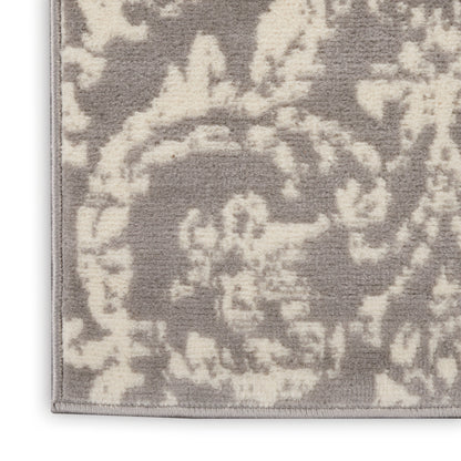 Corner of soft taupe and ivory damask rug with ornate floral pattern and bound trim.