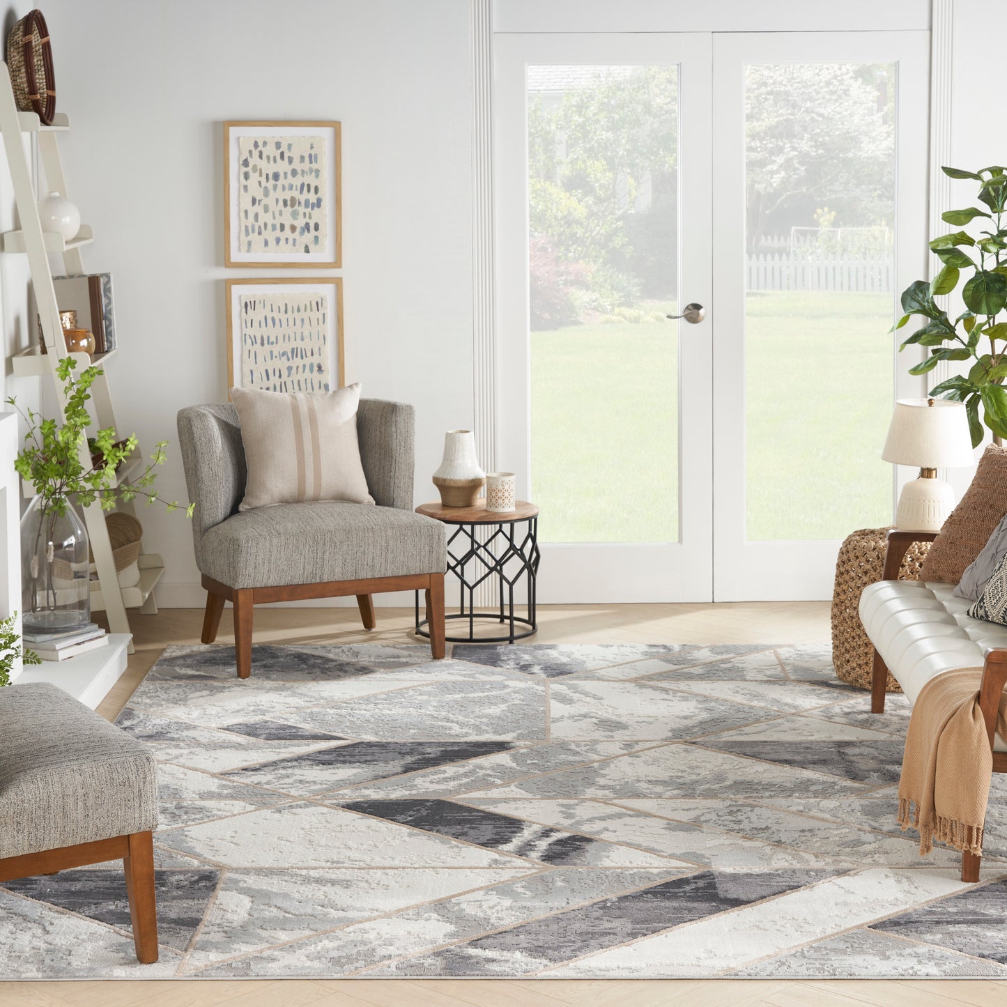Bright living room with grey fabric armchairs, geometric rug, wooden legs, glass French doors, and plants.