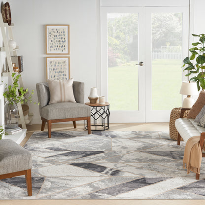 Bright living room with grey fabric armchairs, geometric rug, wooden legs, glass French doors, and plants.