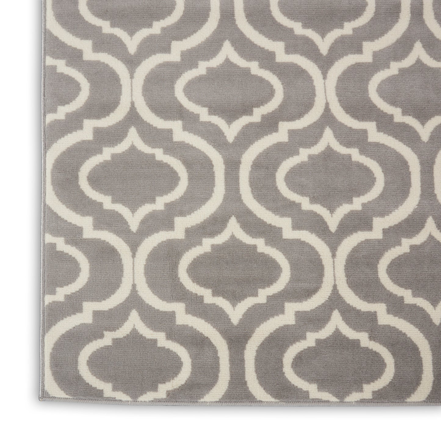 Gray rug with white geometric quatrefoil trellis pattern, woven textile, edge visible.