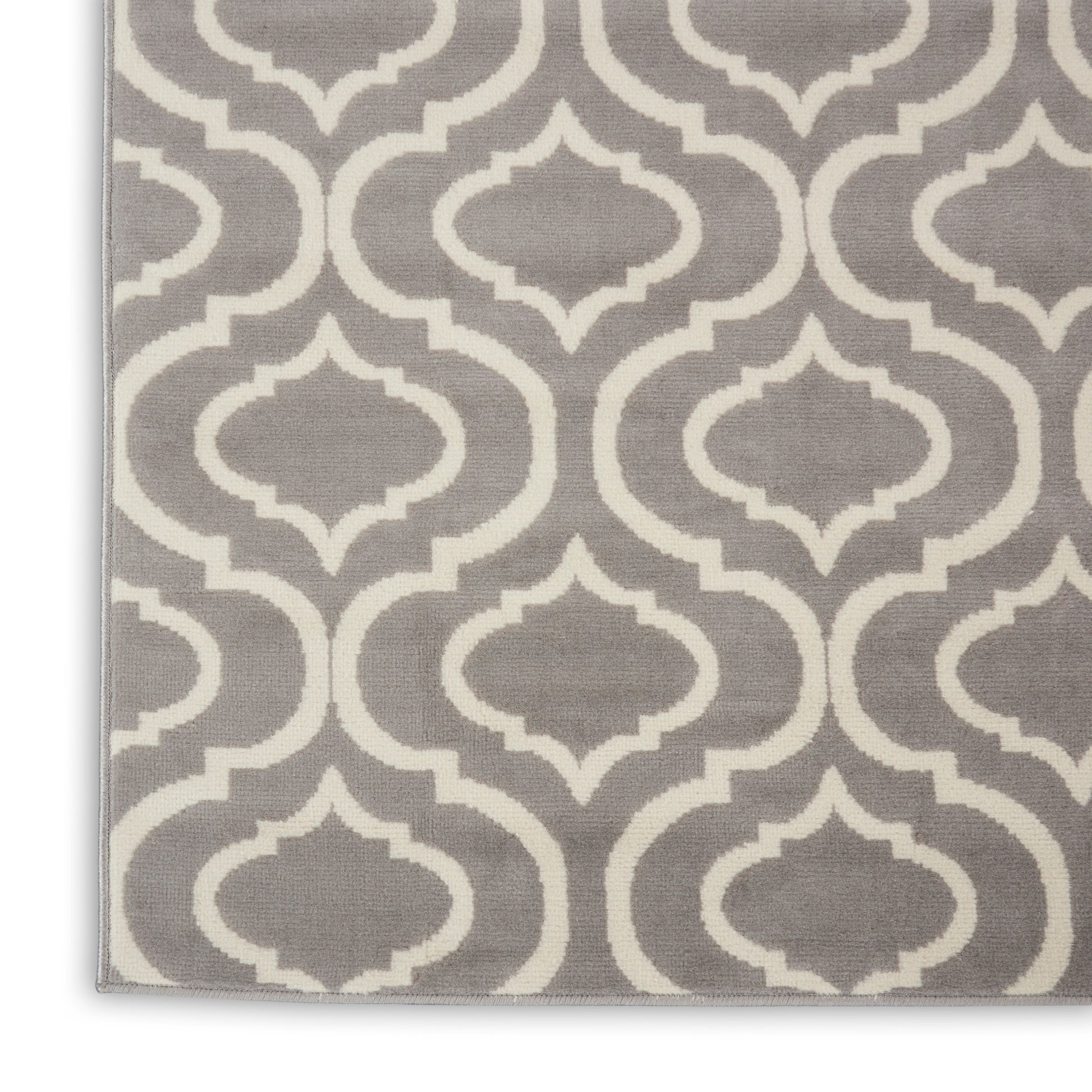 Gray rug with white geometric quatrefoil trellis pattern, woven textile, edge visible.