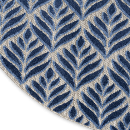 Blue and beige leaf-patterned rug with navy velvet-like leaves on a textured beige background; edge of round rug visible.