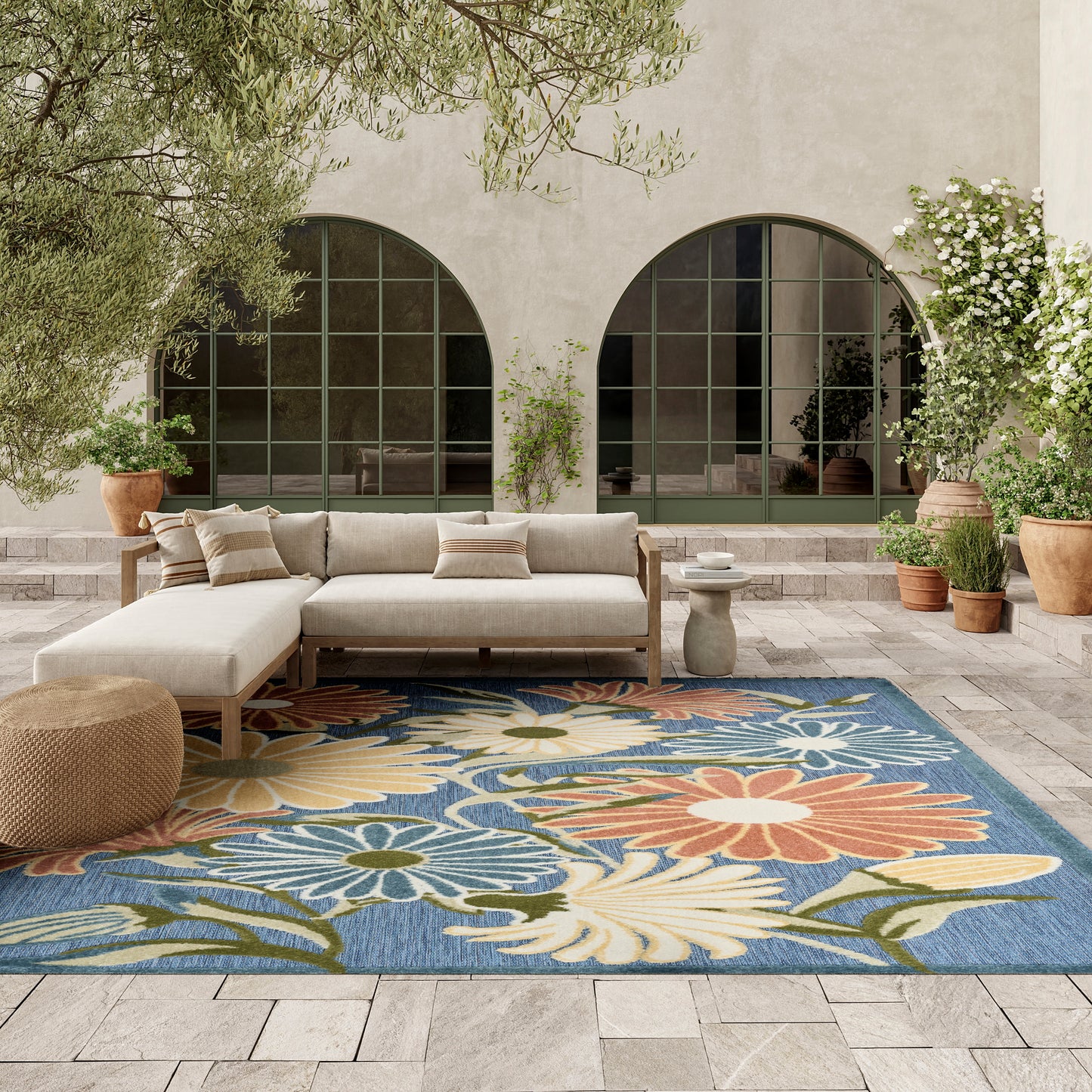 Outdoor rug with a blue floral pattern on a patio, surrounded by potted plants and arched glass doors.