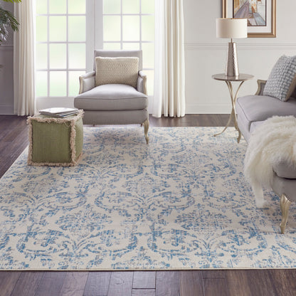 Cozy living room with grey chairs, light sofa, blue-and-cream ornate vintage rug, green fringe ottoman, fur throw, side table.