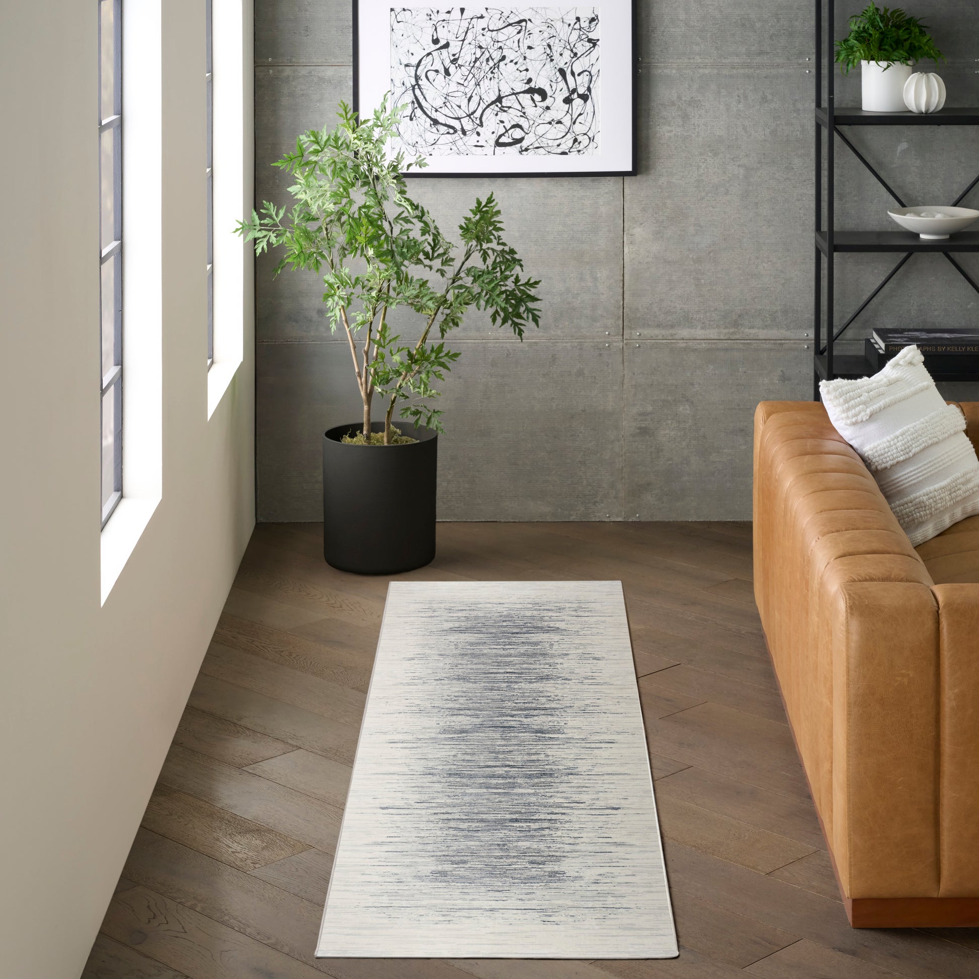 Light gray runner rug with subtle charcoal brushed center, in a modern living room beside a tan leather sofa and plant.
