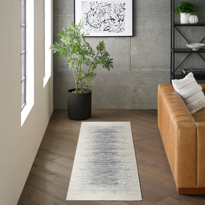 Light gray runner rug with subtle charcoal brushed center, in a modern living room beside a tan leather sofa and plant.