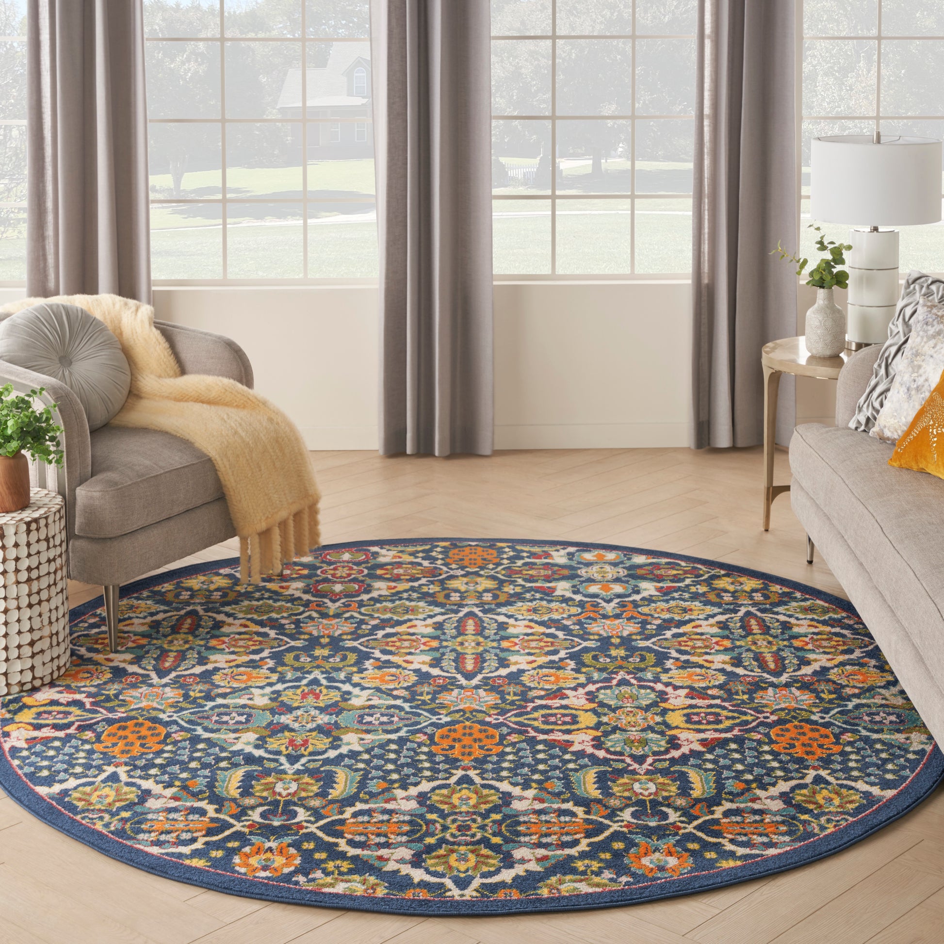 Round navy rug with vivid multicolor floral medallion pattern in a living room with gray sofa, curtains, and wooden floor.