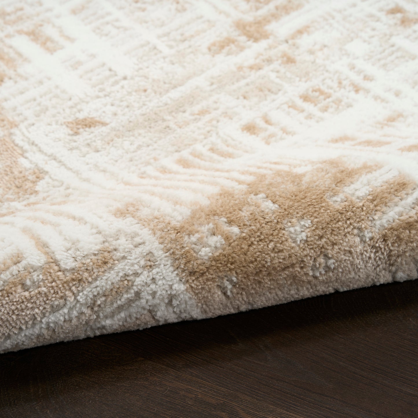 Close-up of a plush beige and white patterned rug edge on dark hardwood floor.