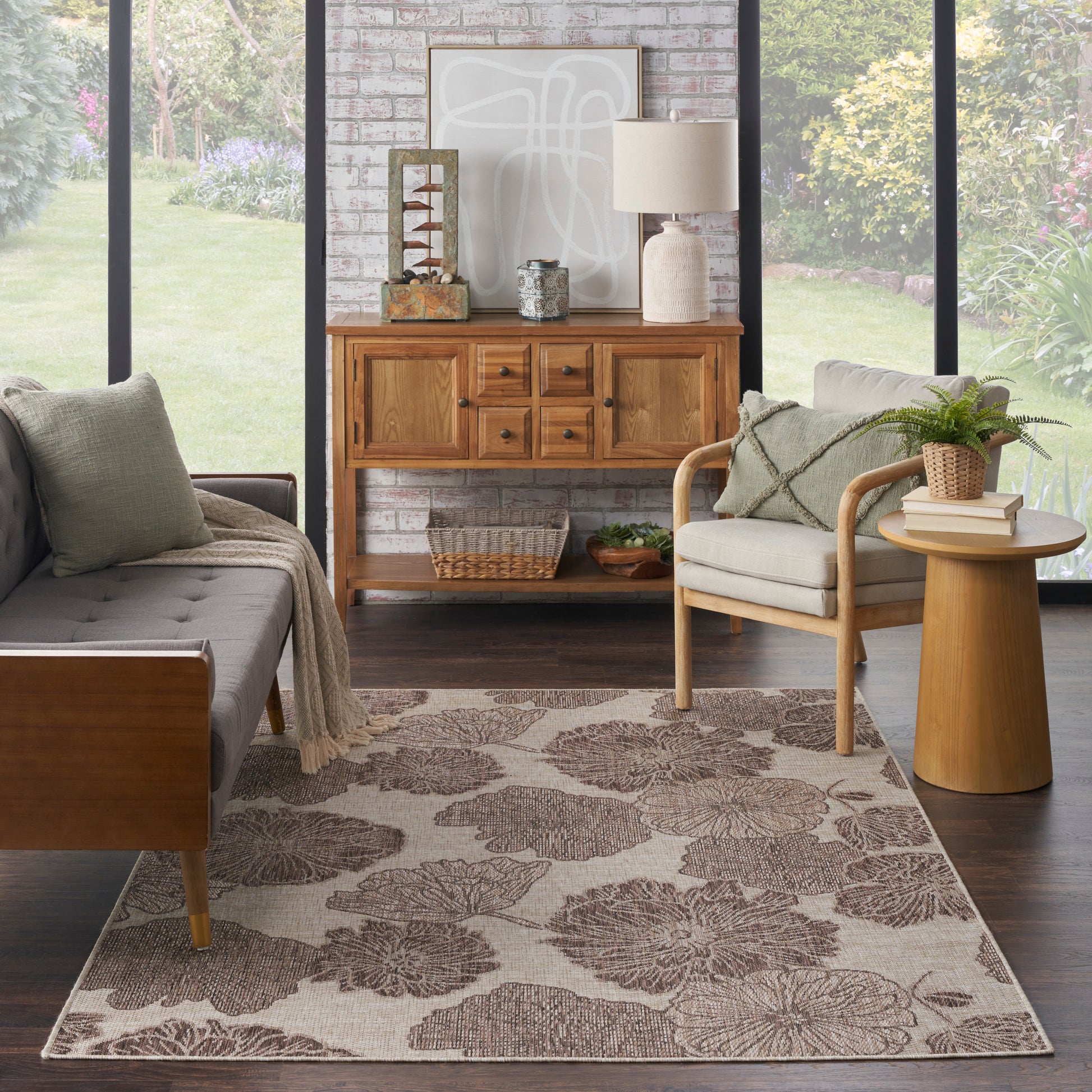 Cozy living room with light wood sofa and chair, gray cushions, round side table, woven basket, floral beige rug, brick wall.