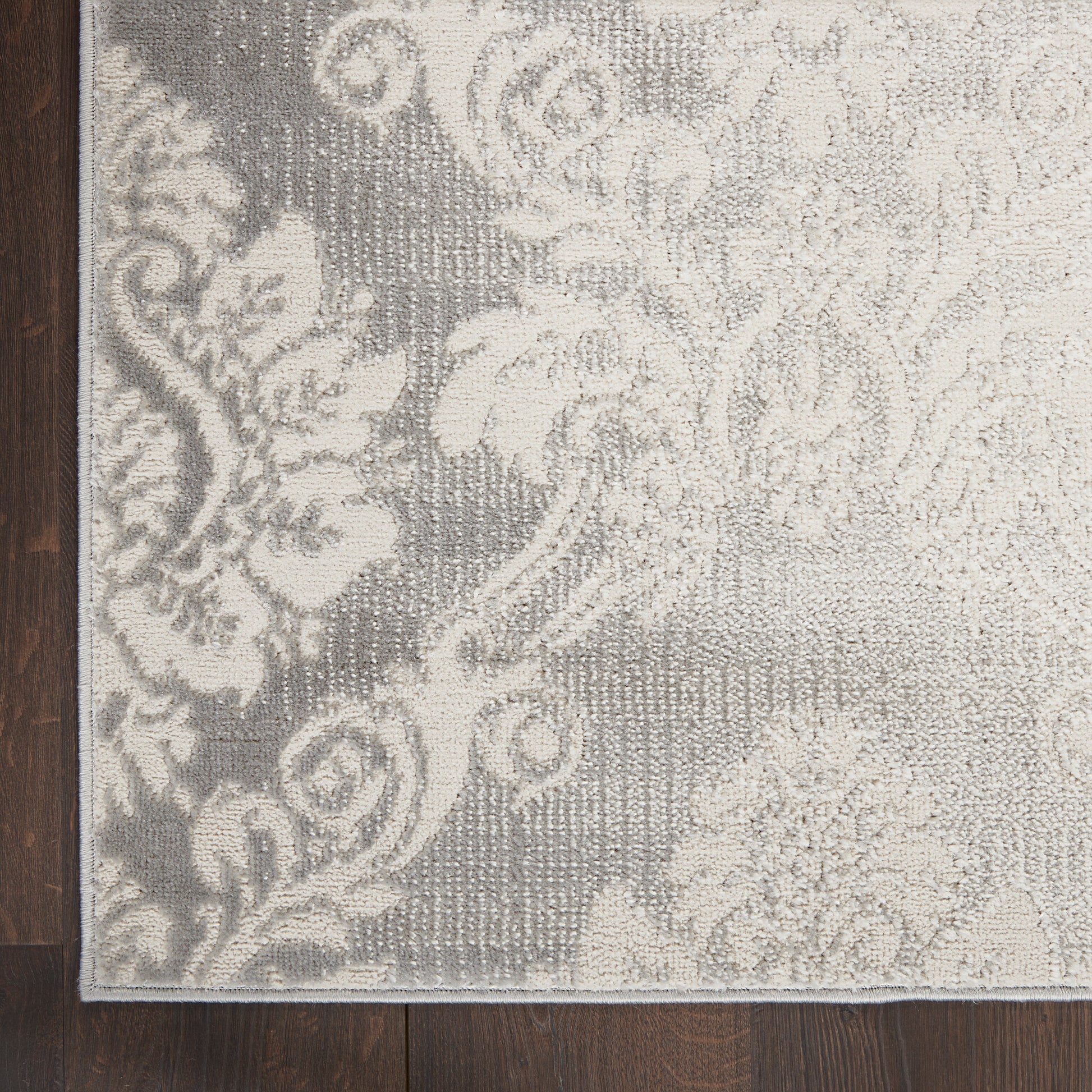 Grey & ivory damask-pattern rug with floral scrolls, rectangular woven rug on dark wood floor.