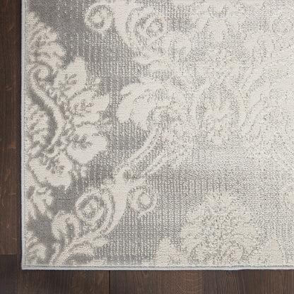 Grey & ivory damask-pattern rug with floral scrolls, rectangular woven rug on dark wood floor.
