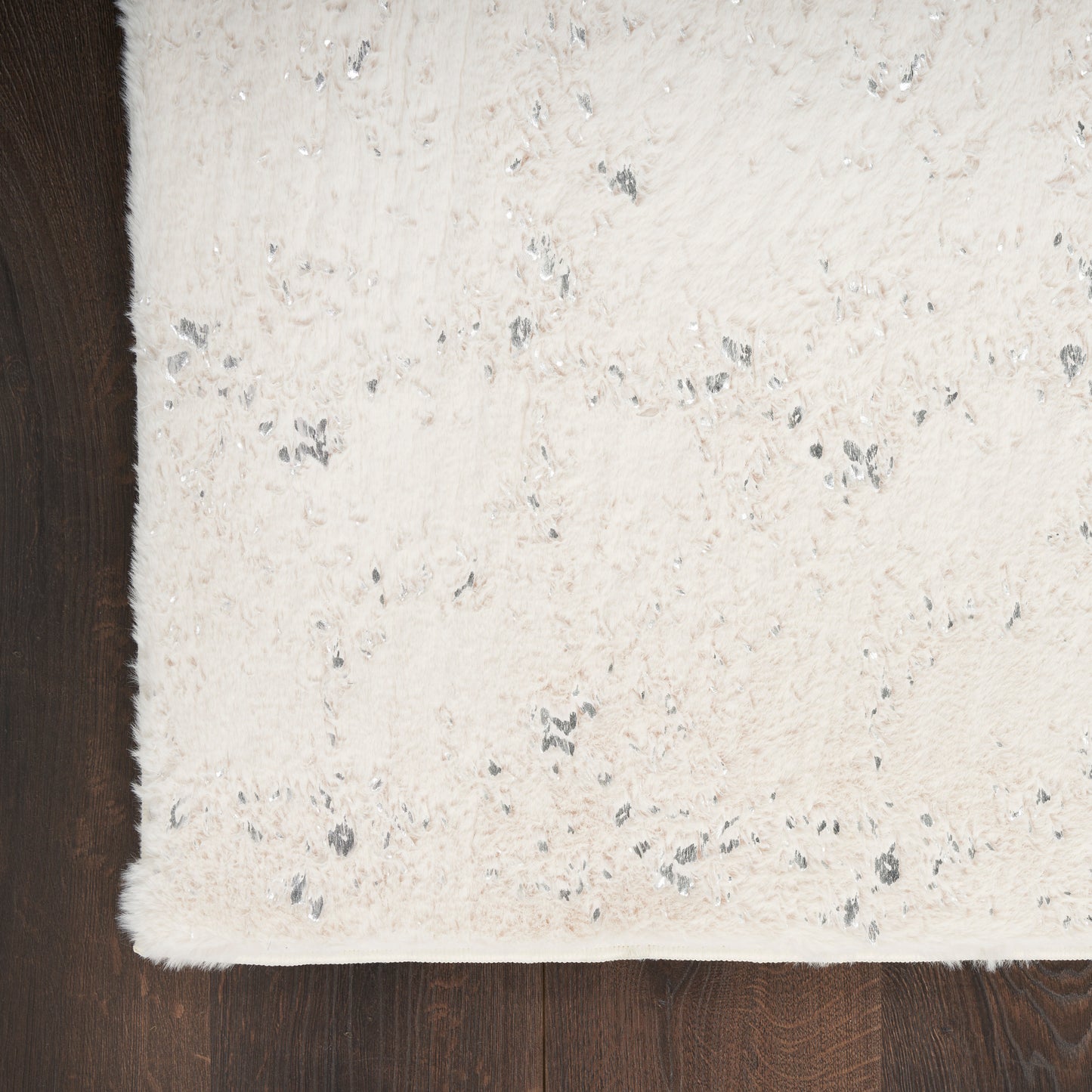 White plush rug with gray speckles on dark wood floor; soft, rectangular area rug.