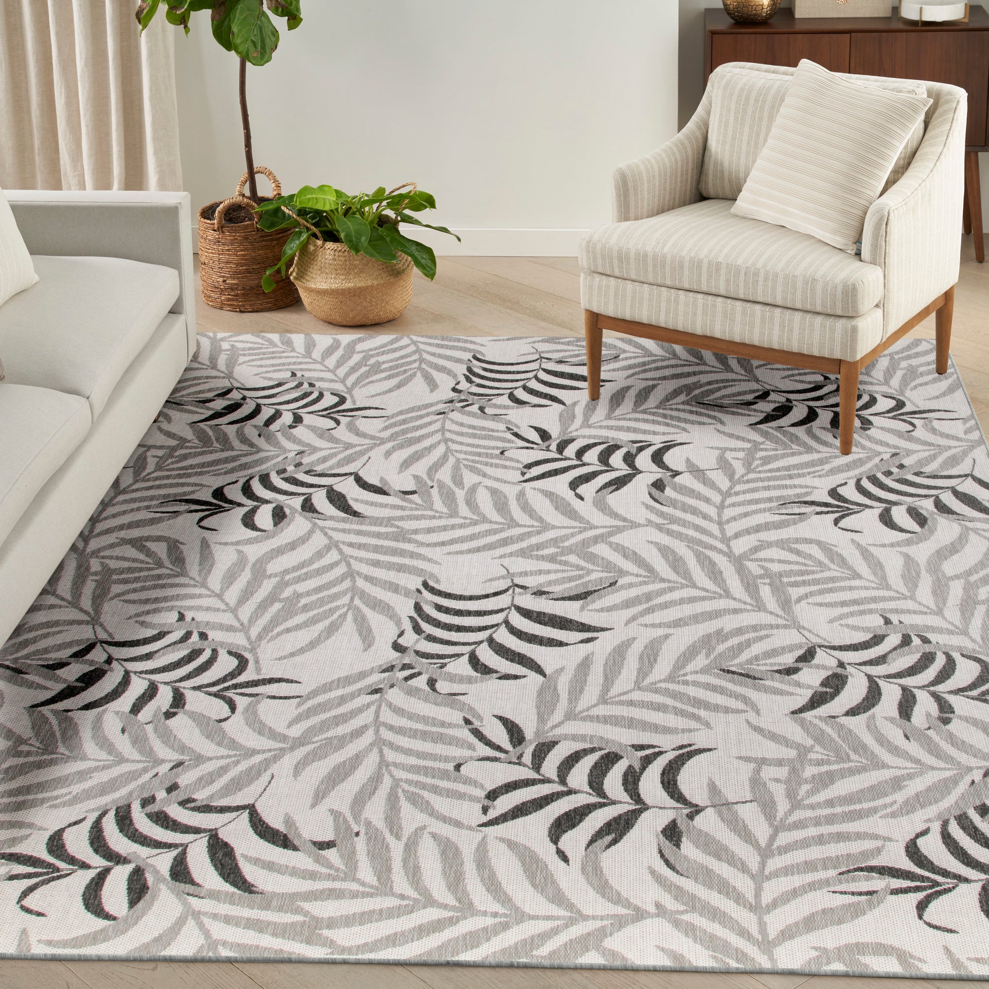 Light gray area rug with black fern leaf pattern in a modern living room; cream sofa, striped armchair, and potted plants.