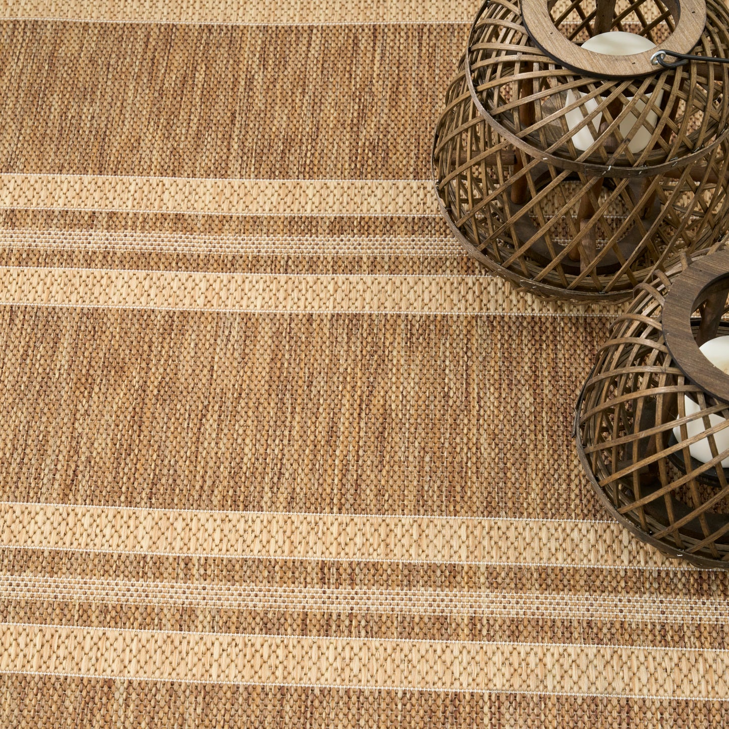 Beige-tan striped jute rug with two dark brown spherical rattan lanterns and candles.