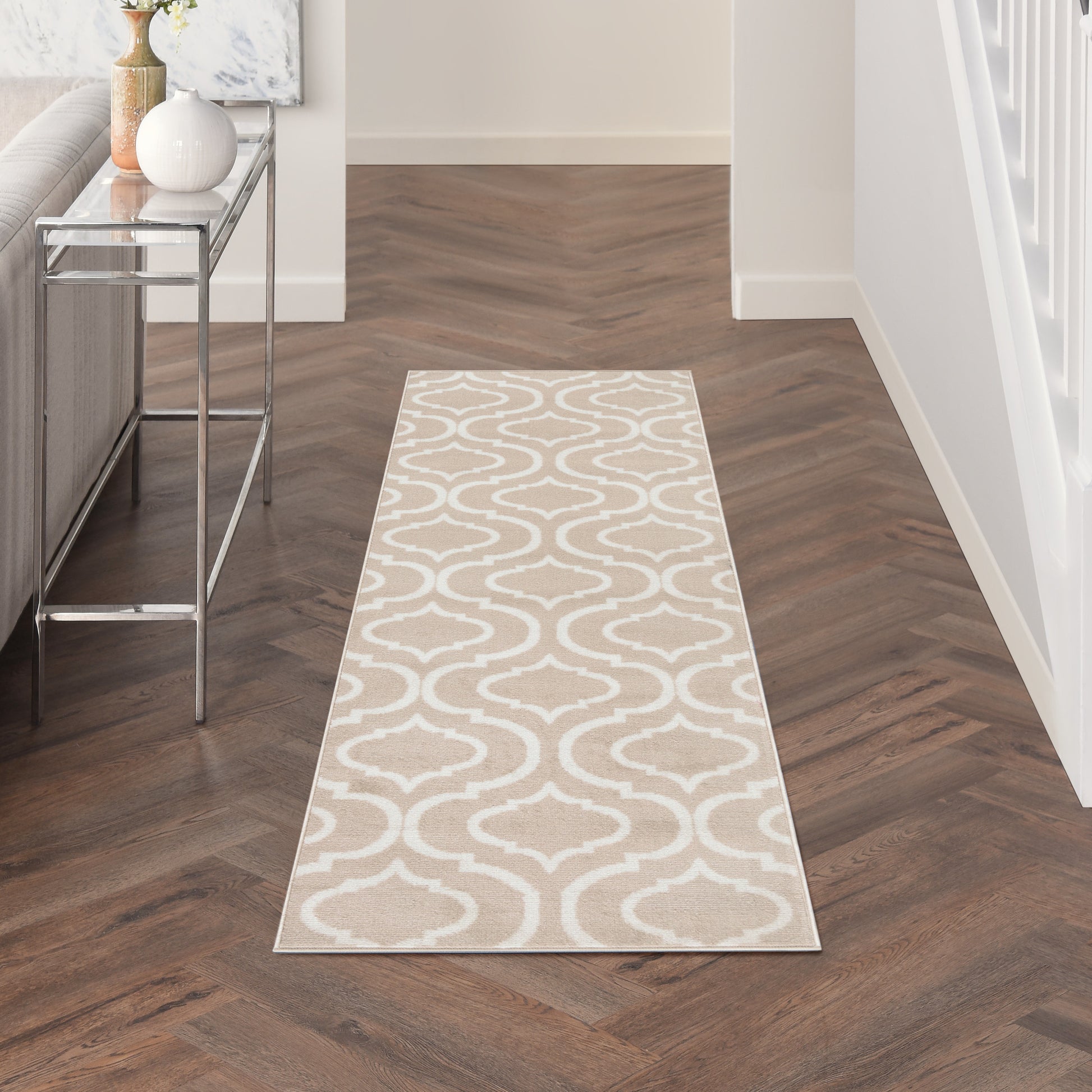 Beige runner rug with white interlocking arabesque pattern in a dark wood hallway; chrome-glass console on the left.