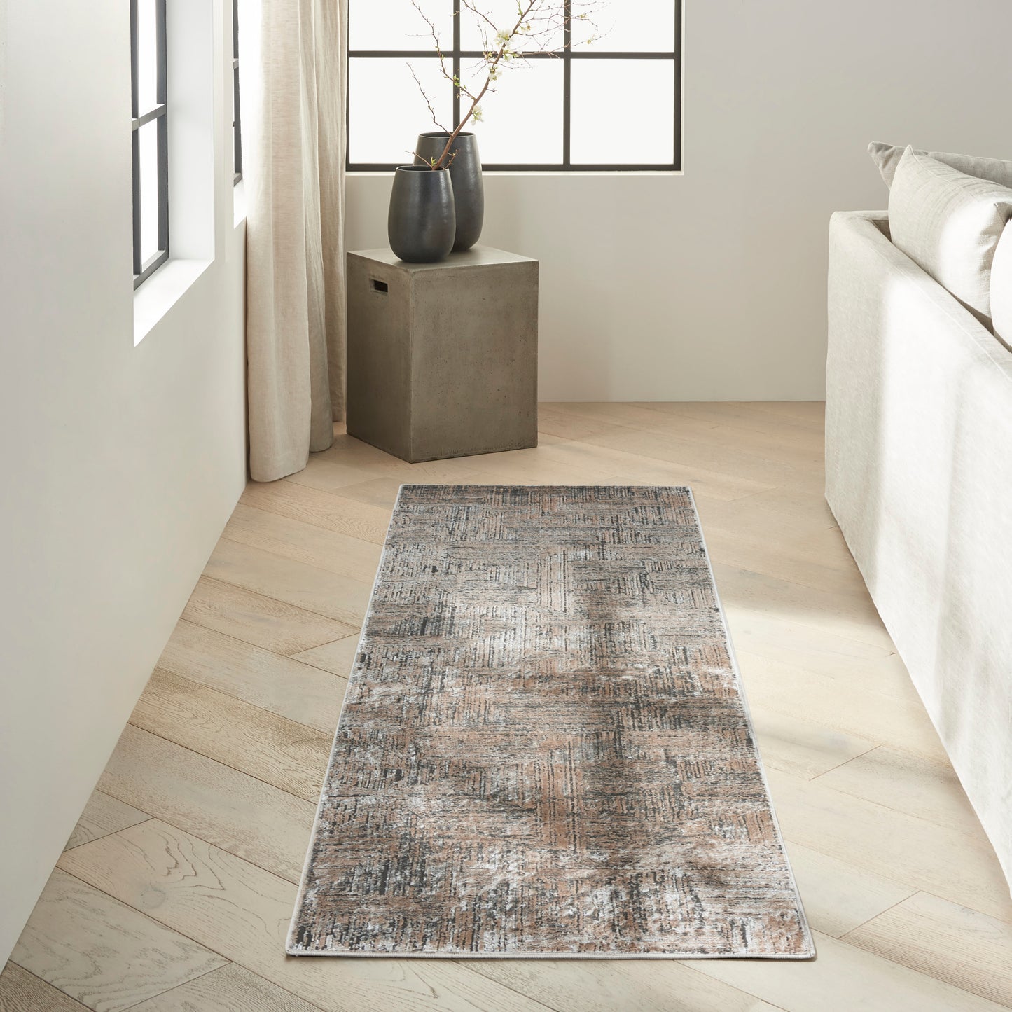 Rectangular distressed gray-blue rug on light wood floor beside a cream sofa and dark cube side table with vases.