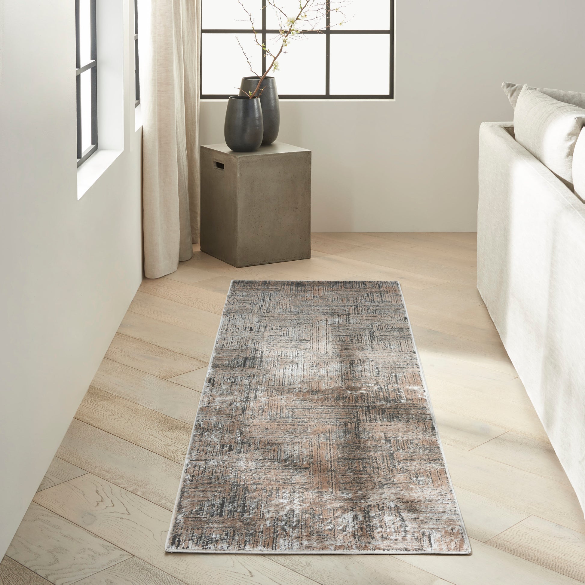 Rectangular distressed gray-blue rug on light wood floor beside a cream sofa and dark cube side table with vases.
