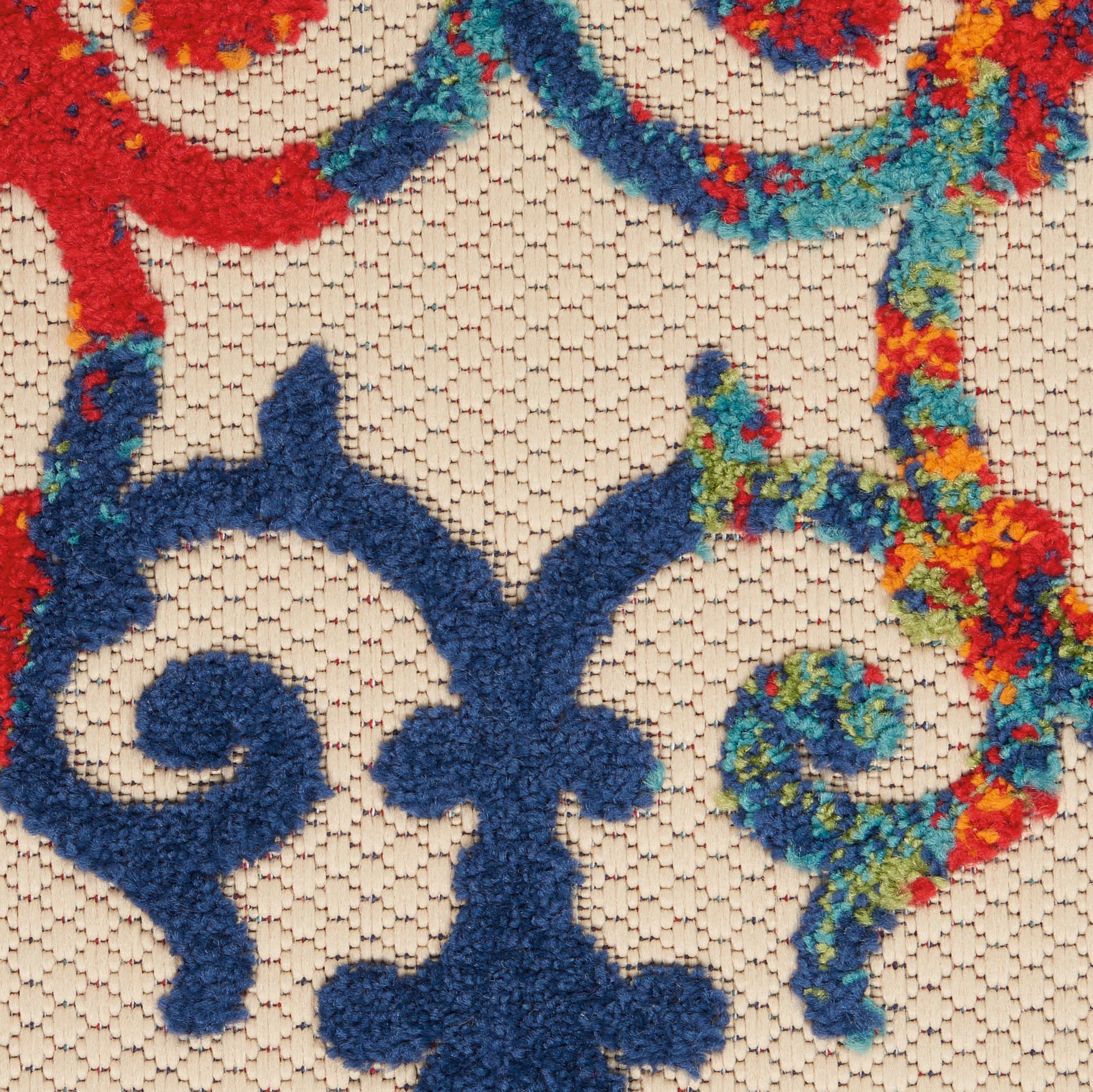 Beige tufted rug with bold blue fleur-de-lis motif and vivid multicolor border in red, teal, green and orange.