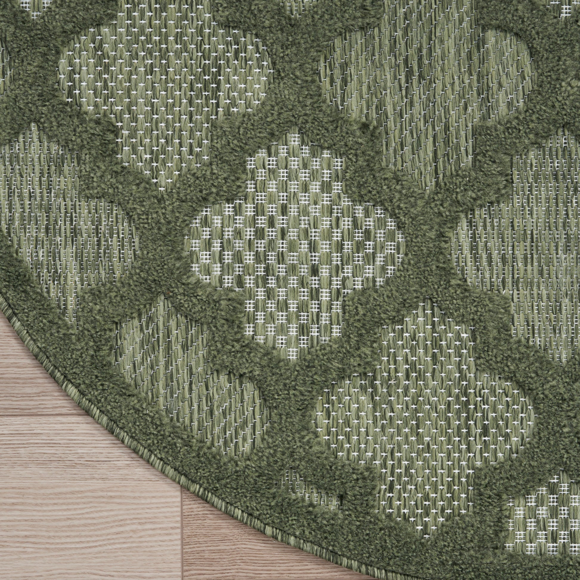Matte olive-green square panel on wooden floor, with green patterned rug edge; modern decorative accent.