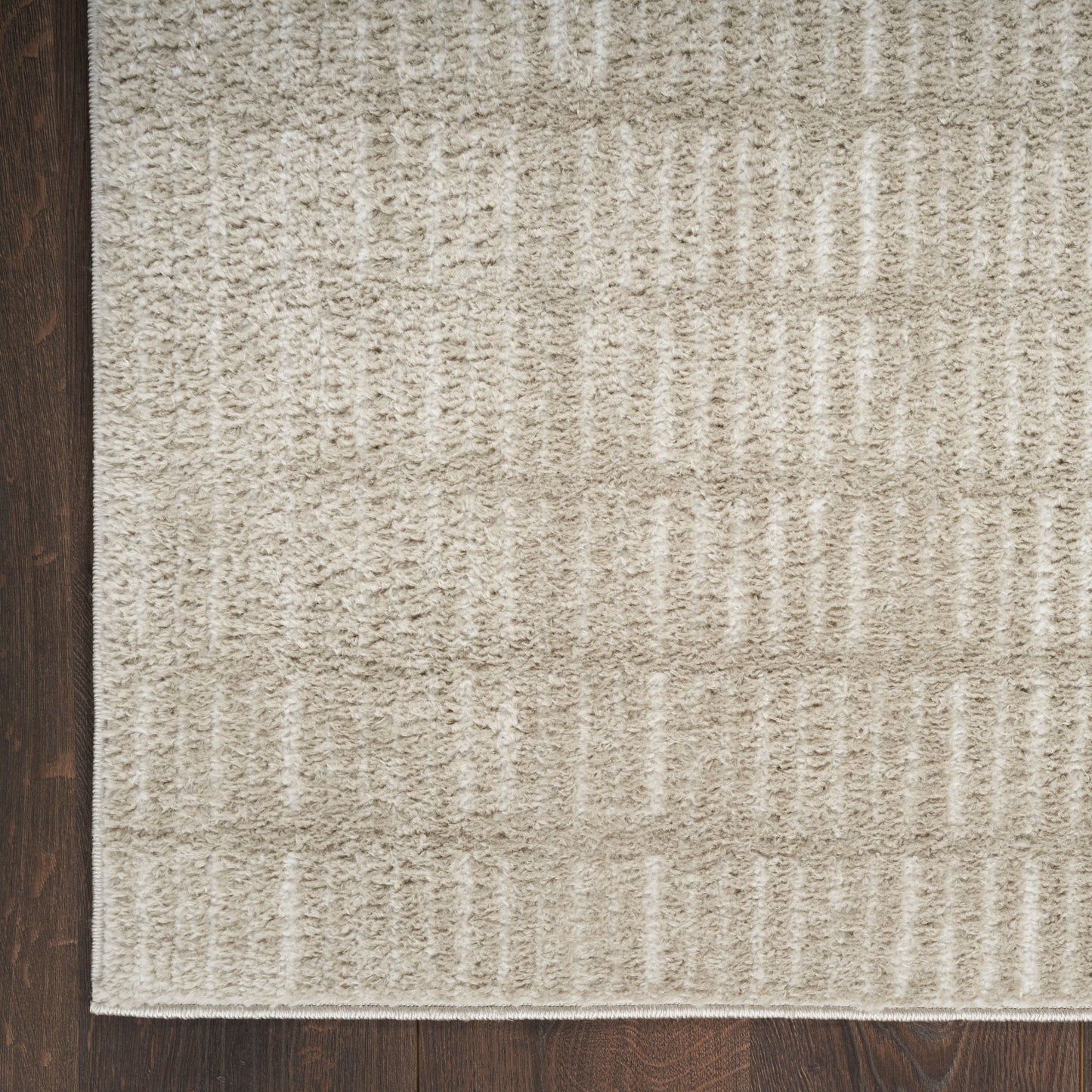 Beige textured area rug with a geometric block pattern on a dark wood floor.