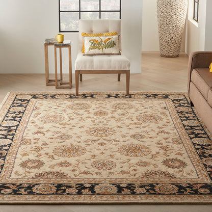 Beige oriental area rug with floral medallions and navy border; living room scene with light wood floor and cream chair.