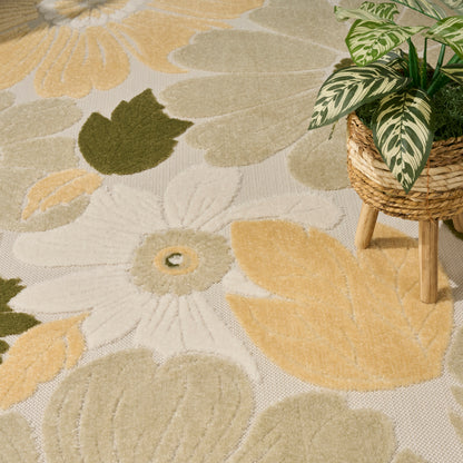 Cream and yellow floral area rug with olive green leaves; potted leafy plant on a woven wicker stand.
