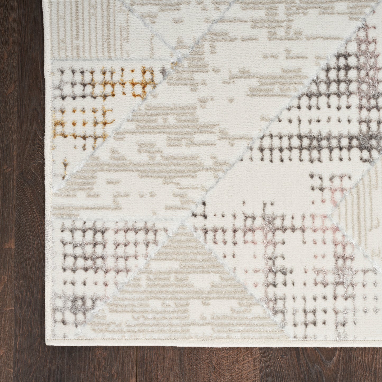 Geometric runner rug with cream, beige and gray patchwork triangles on dark wood floor; soft woven style.