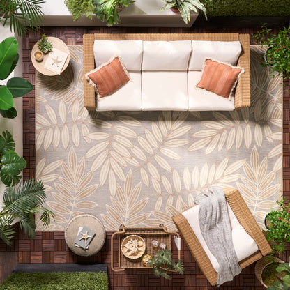 Outdoor wicker sofa with beige cushions on a leaf-print rug, orange pillows, and a matching lounge chair with plants nearby