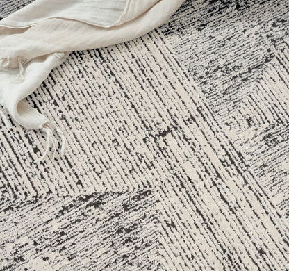 Neutral ivory and charcoal striped rug with a textured weave; cream linen draped at the edge.